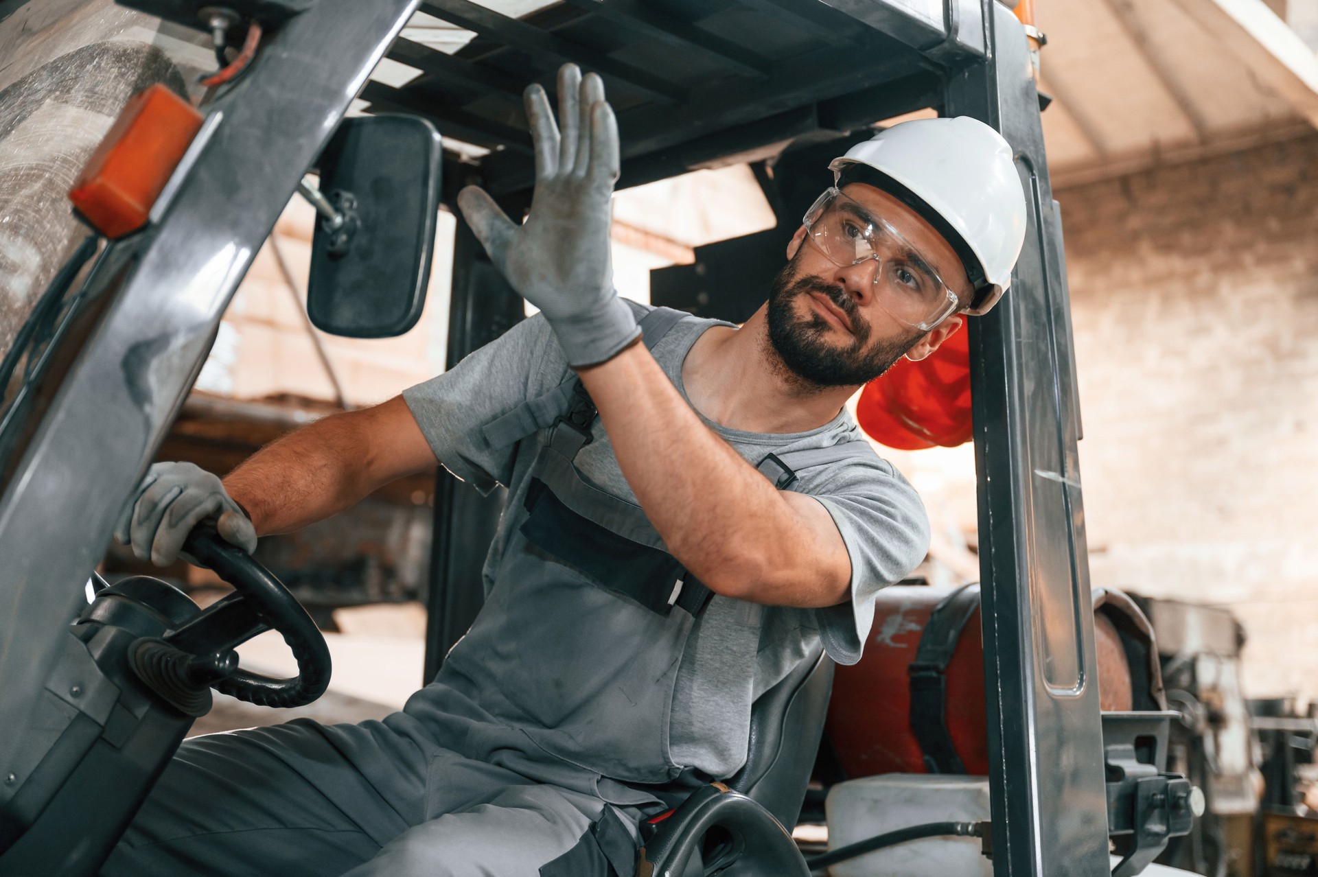 Hand gestures. In the forklift. Young factory worker in grey uniform